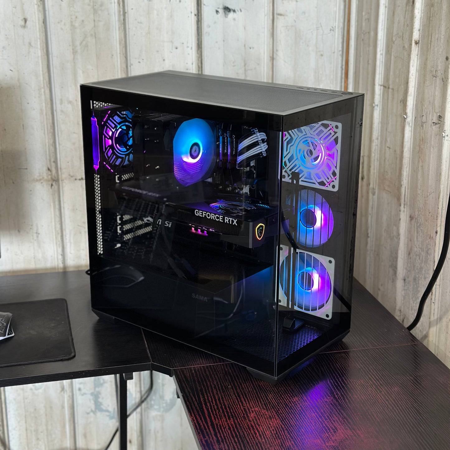 Gaming computer tower with RGB lighting on a desk against a wooden wall.