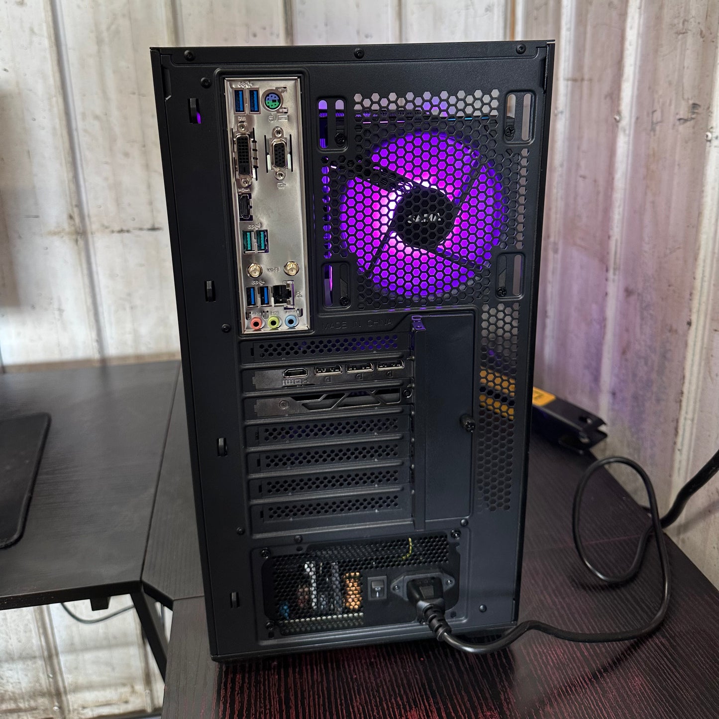 Back view of a computer case with a purple cooling fan on a desk.