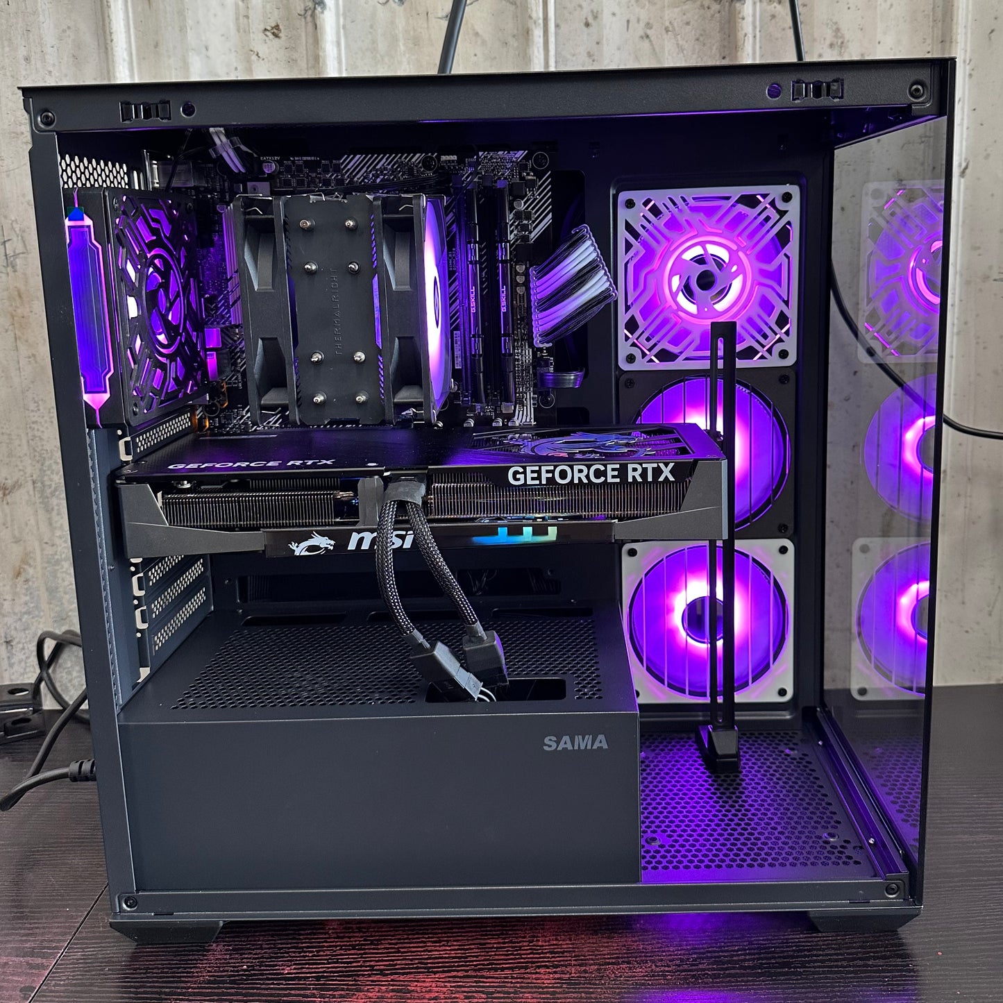 Open computer case with visible components and purple lighting on a wooden surface.