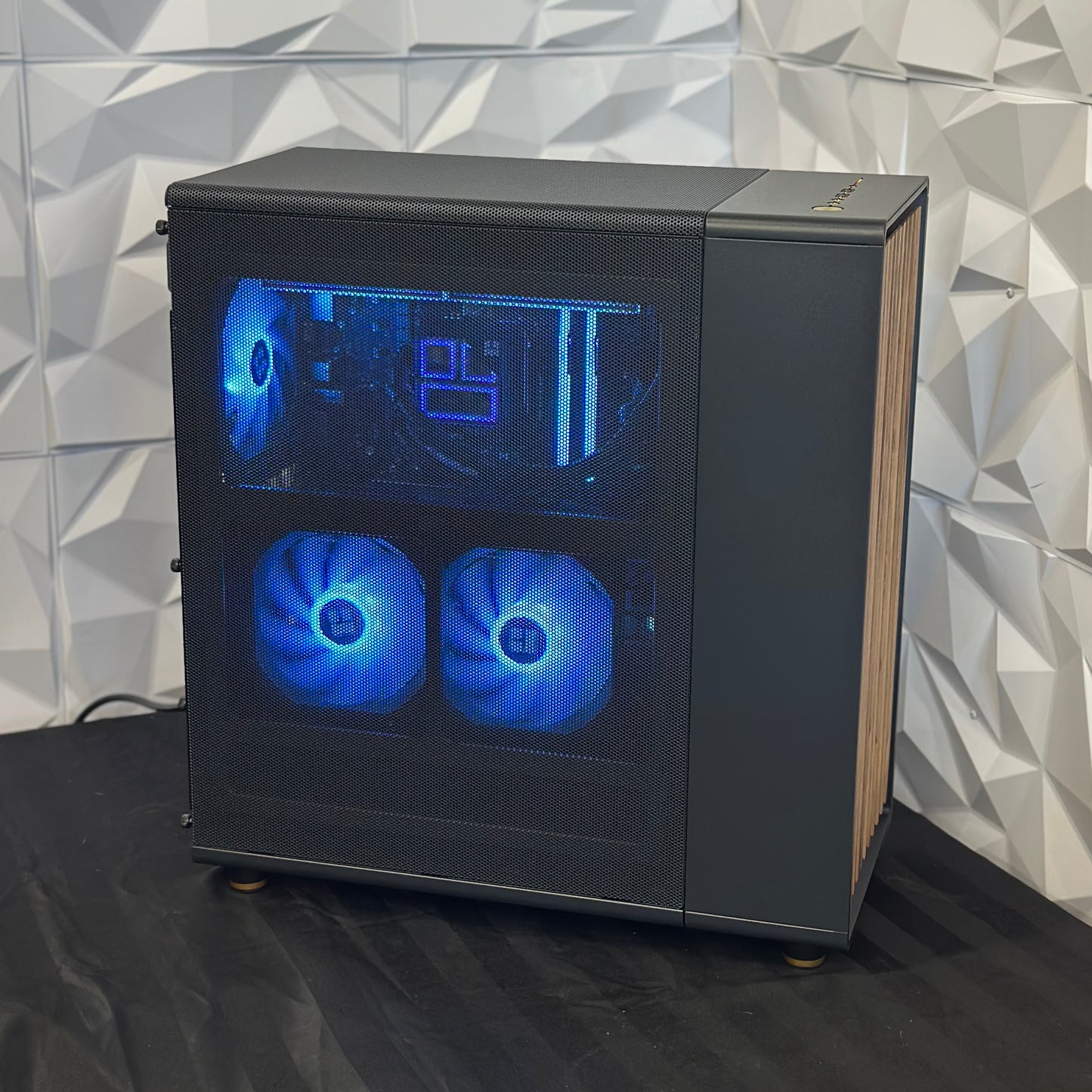 Computer case with blue LED fans on a black surface against a geometric-patterned wall.
