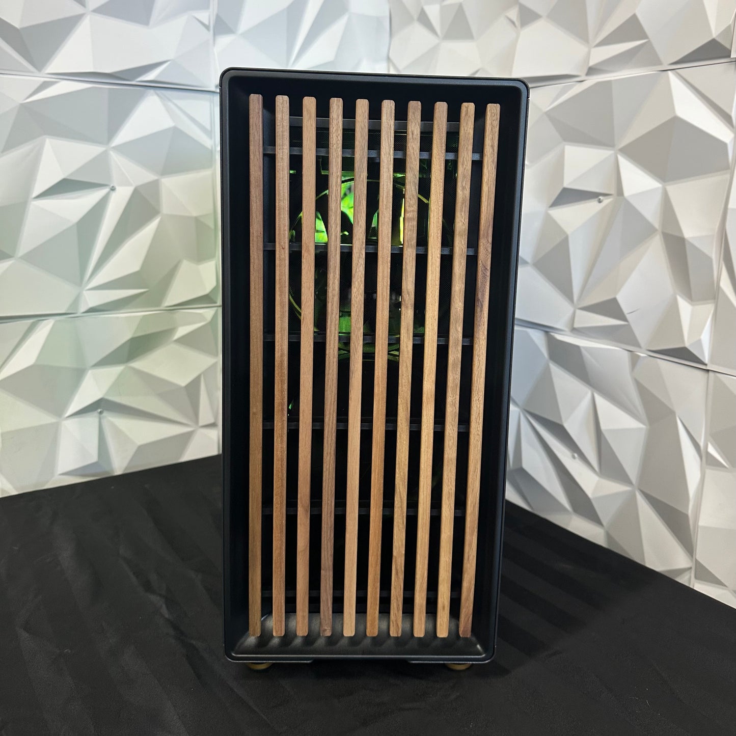 Black rectangular object with wooden slats against a geometric-patterned wall.