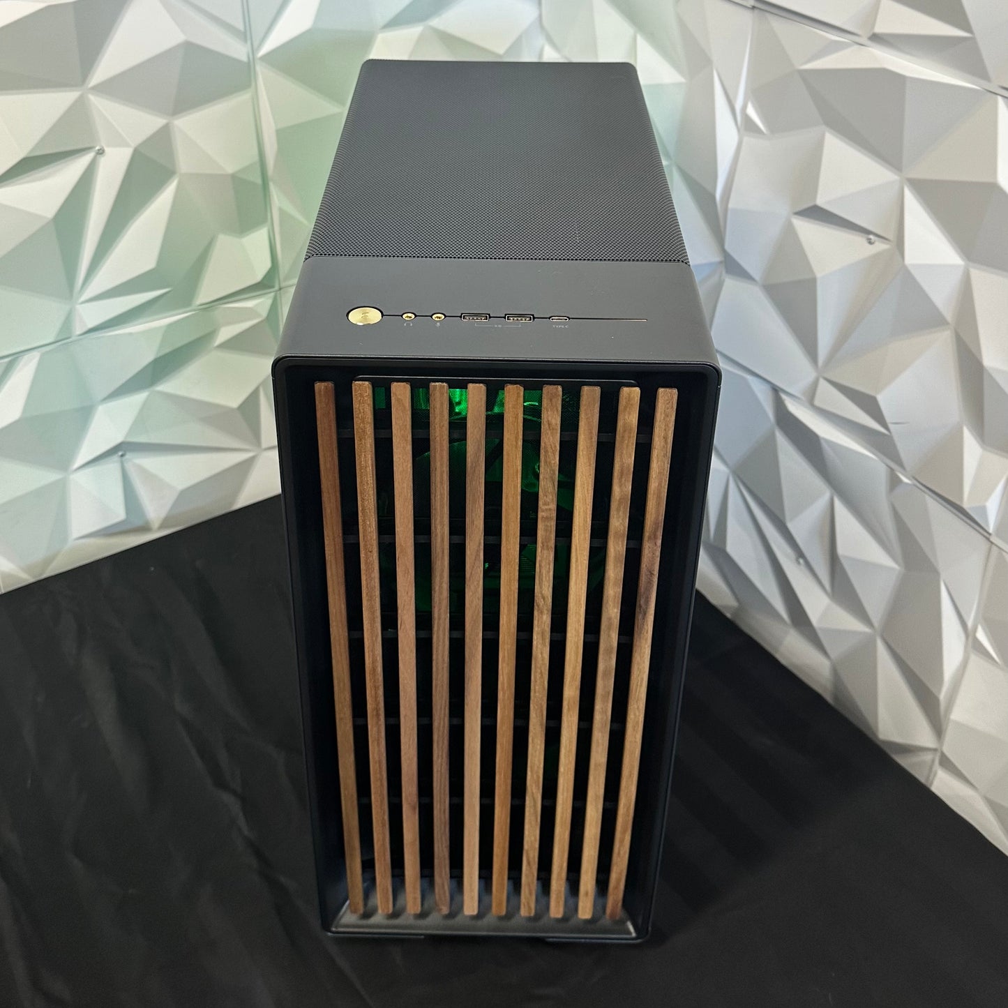 Black computer case with wooden side panel against a geometric patterned wall.