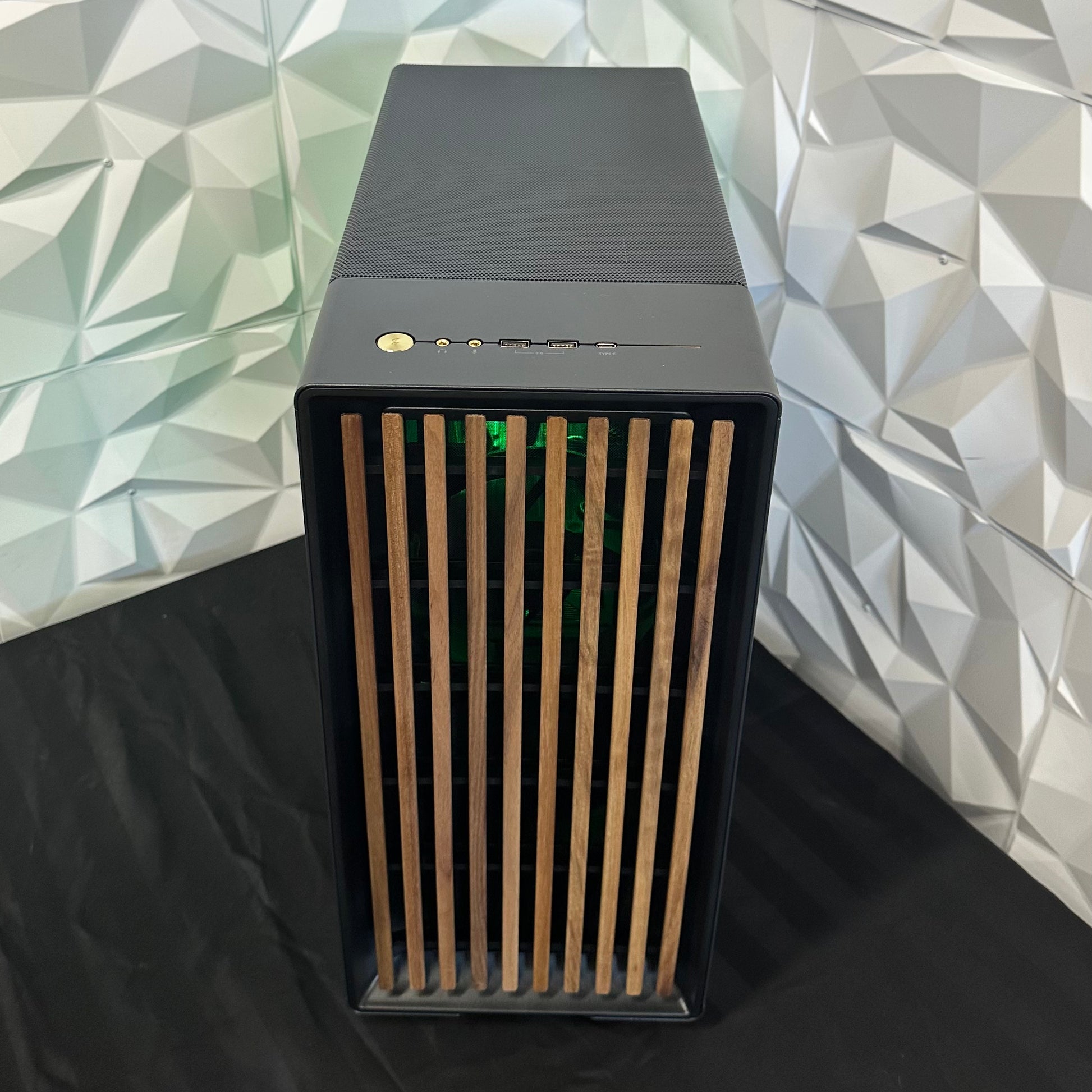 Black computer case with wooden side panel against a geometric patterned wall.