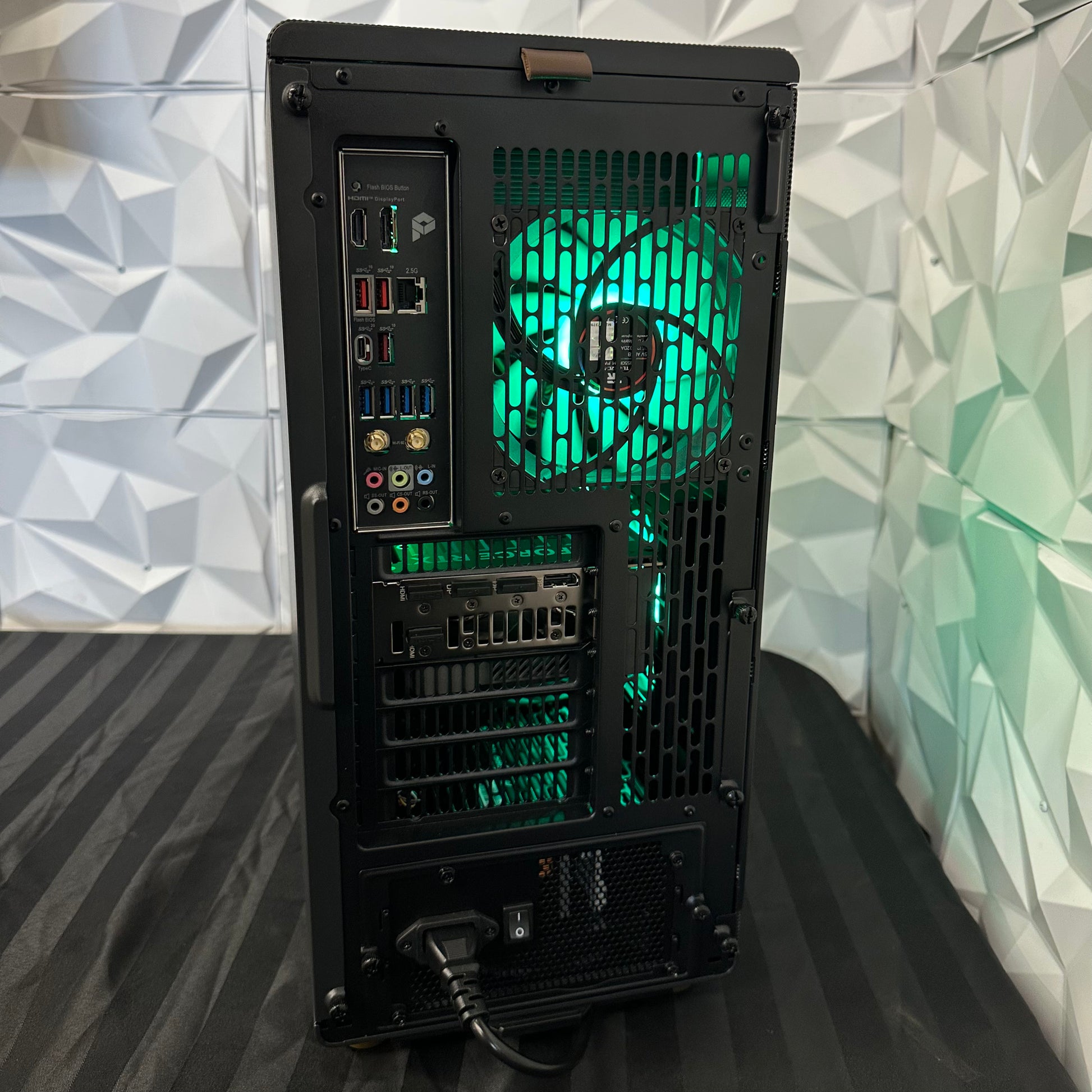 Back view of a computer case with green lighting against a geometric patterned wall.