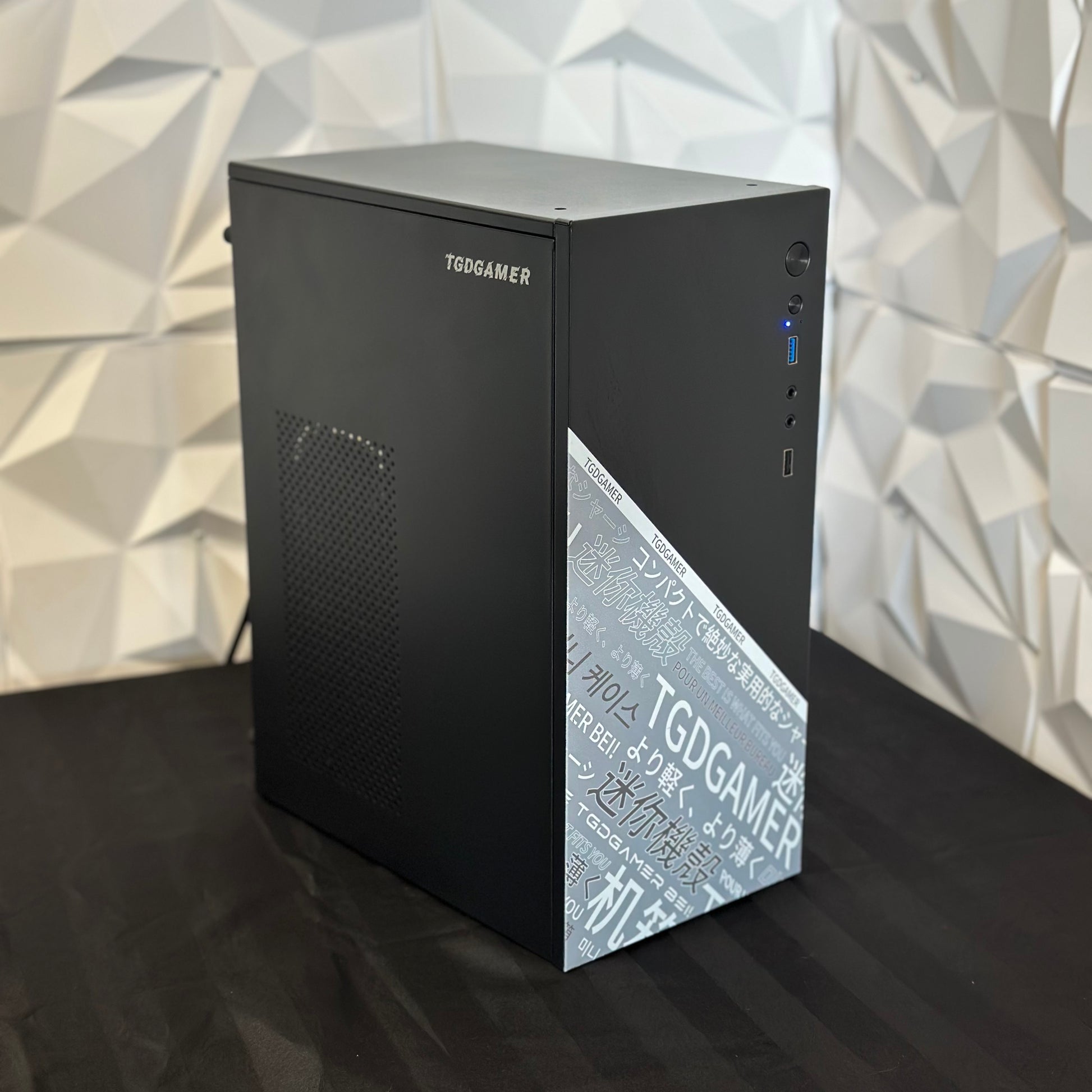 Black computer case with TGD GAMER branding on a reflective surface with geometric wall background