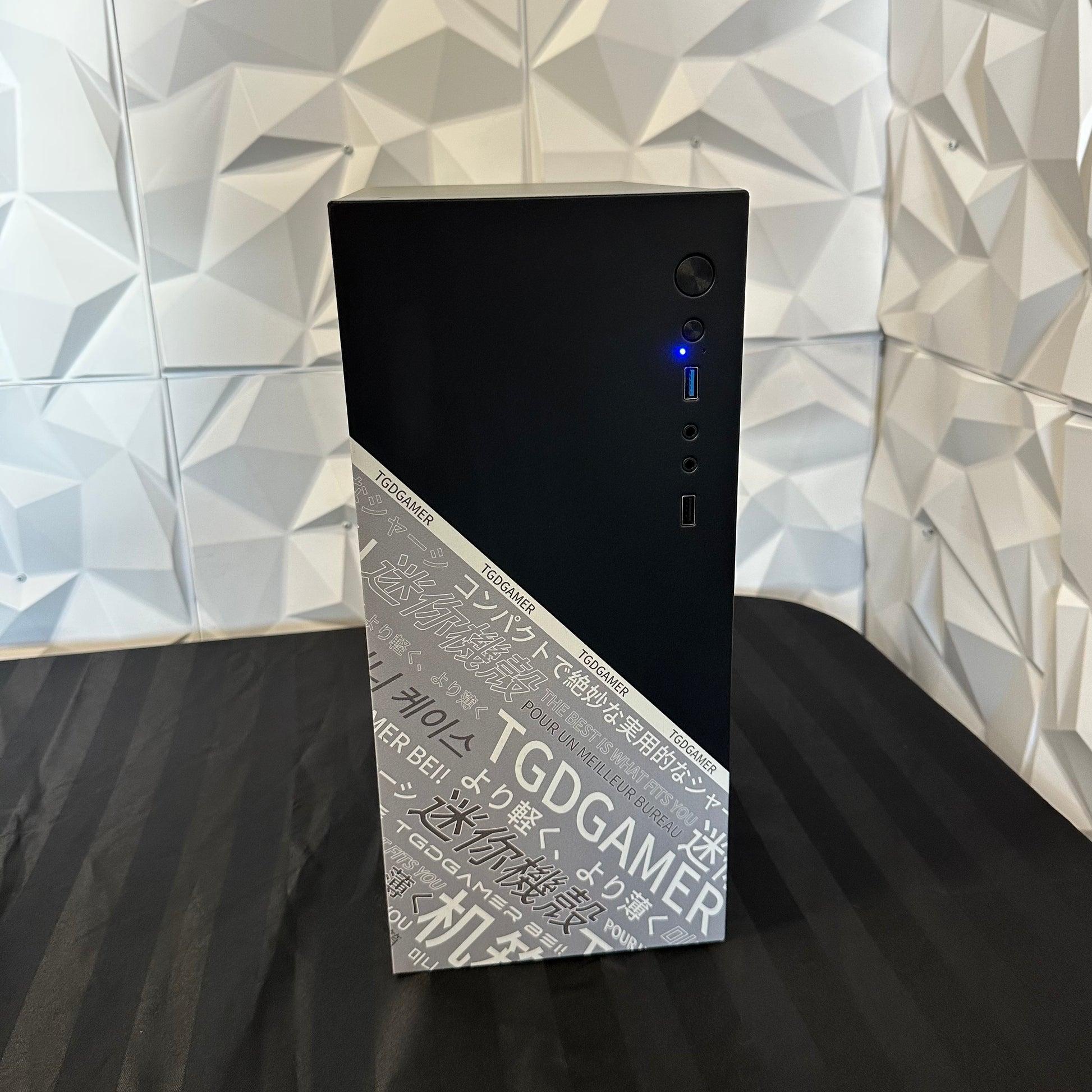 TGDGAMER computer tower with Japanese text on a black surface against a geometric-patterned wall.
