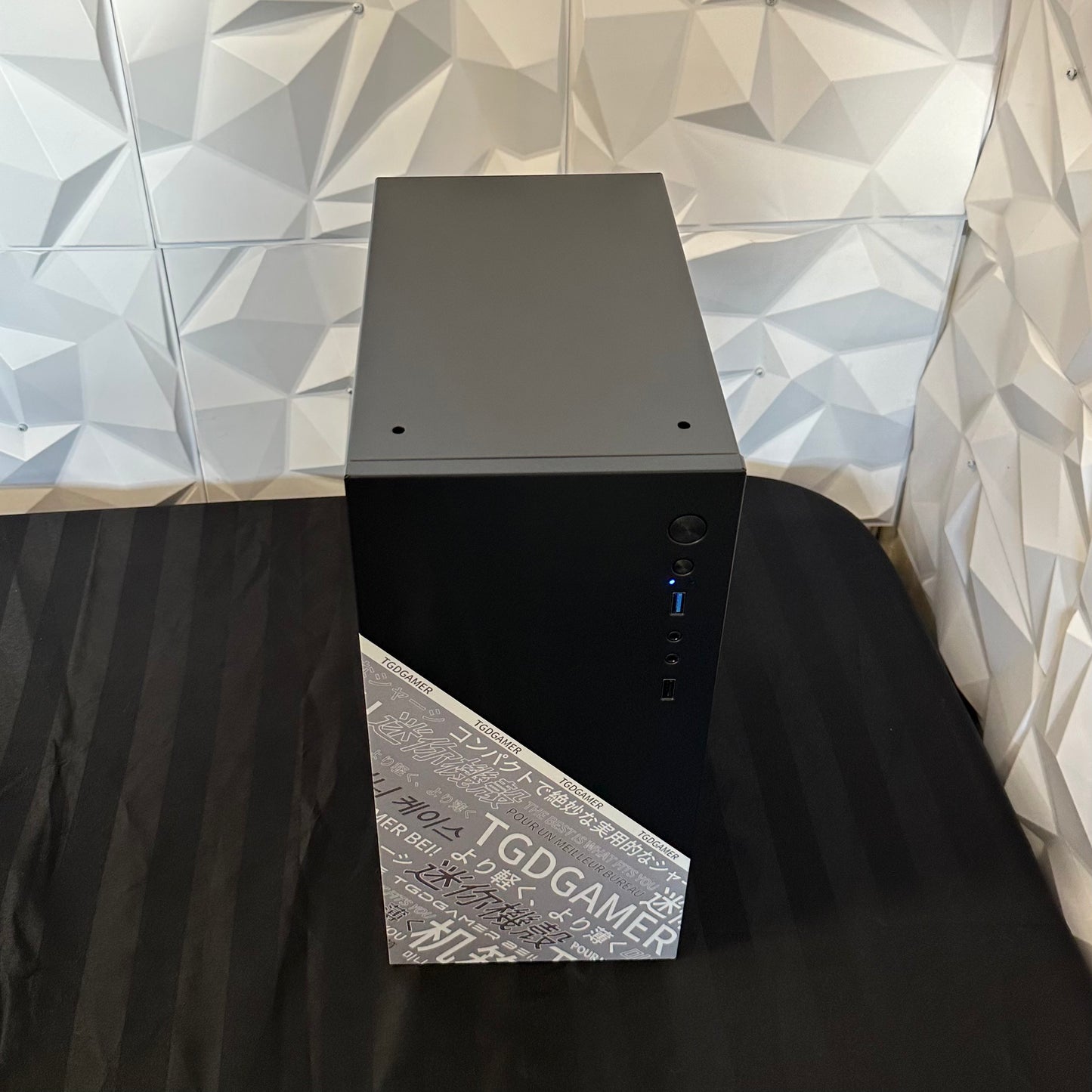 Black computer tower on a black surface with a geometric-patterned wall in the background