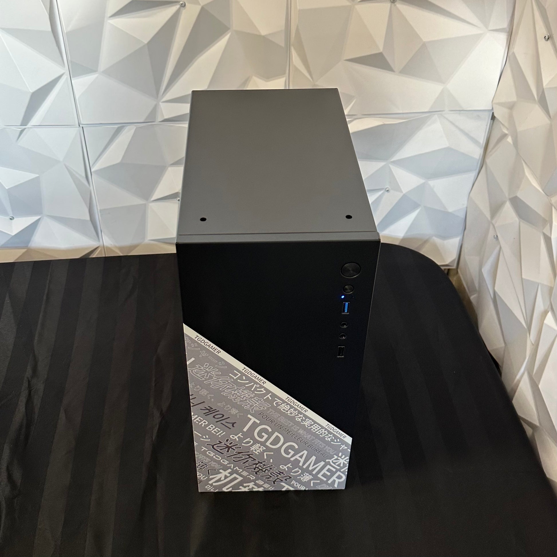 Black computer tower on a black surface with a geometric-patterned wall in the background