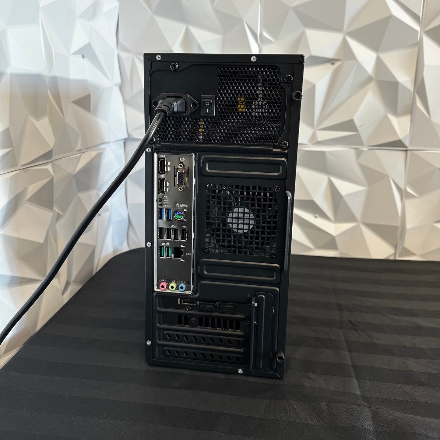 Black computer tower on a black surface with a geometric patterned wall in the background