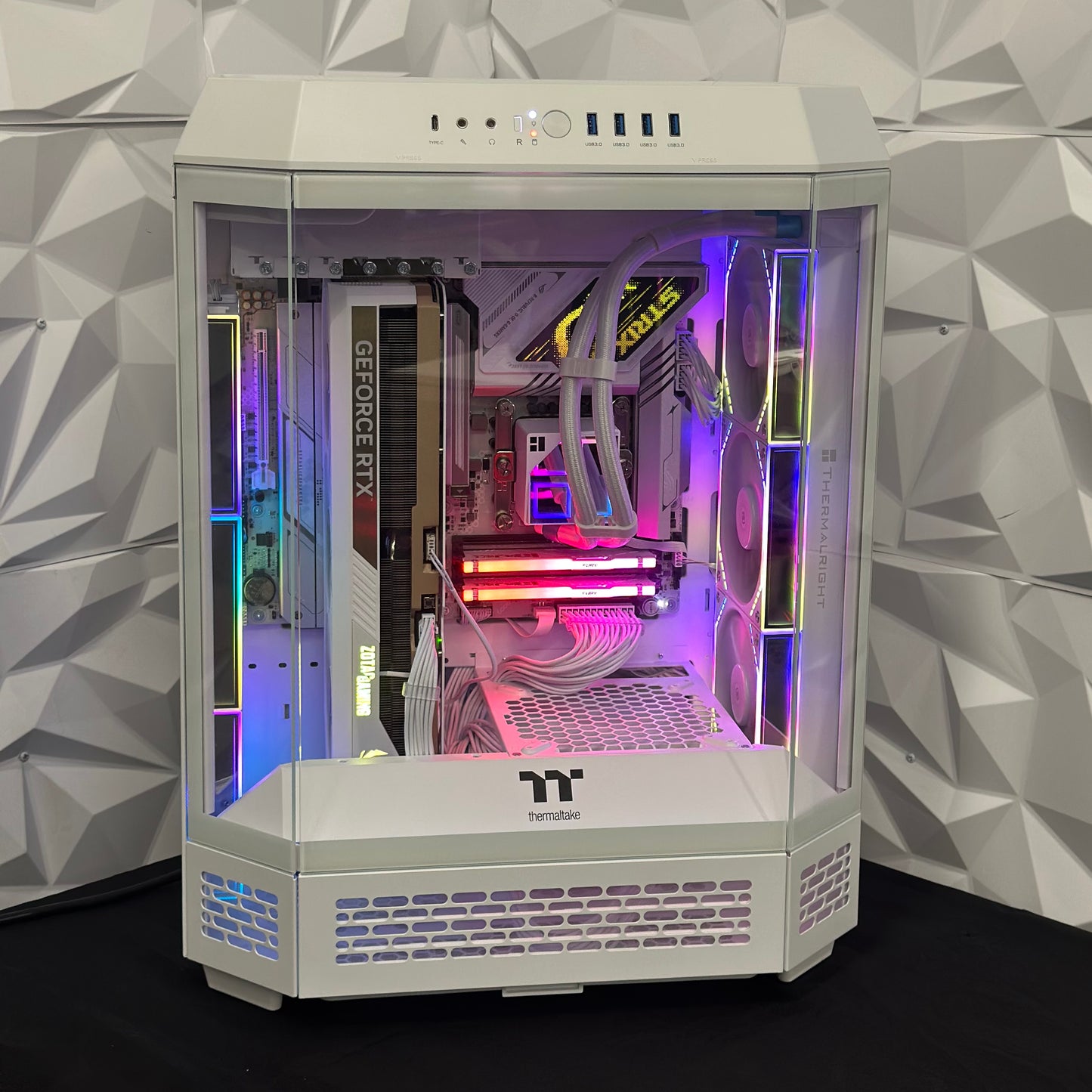Computer gaming PC with RGB lighting inside a white case against a geometric-patterned wall.
