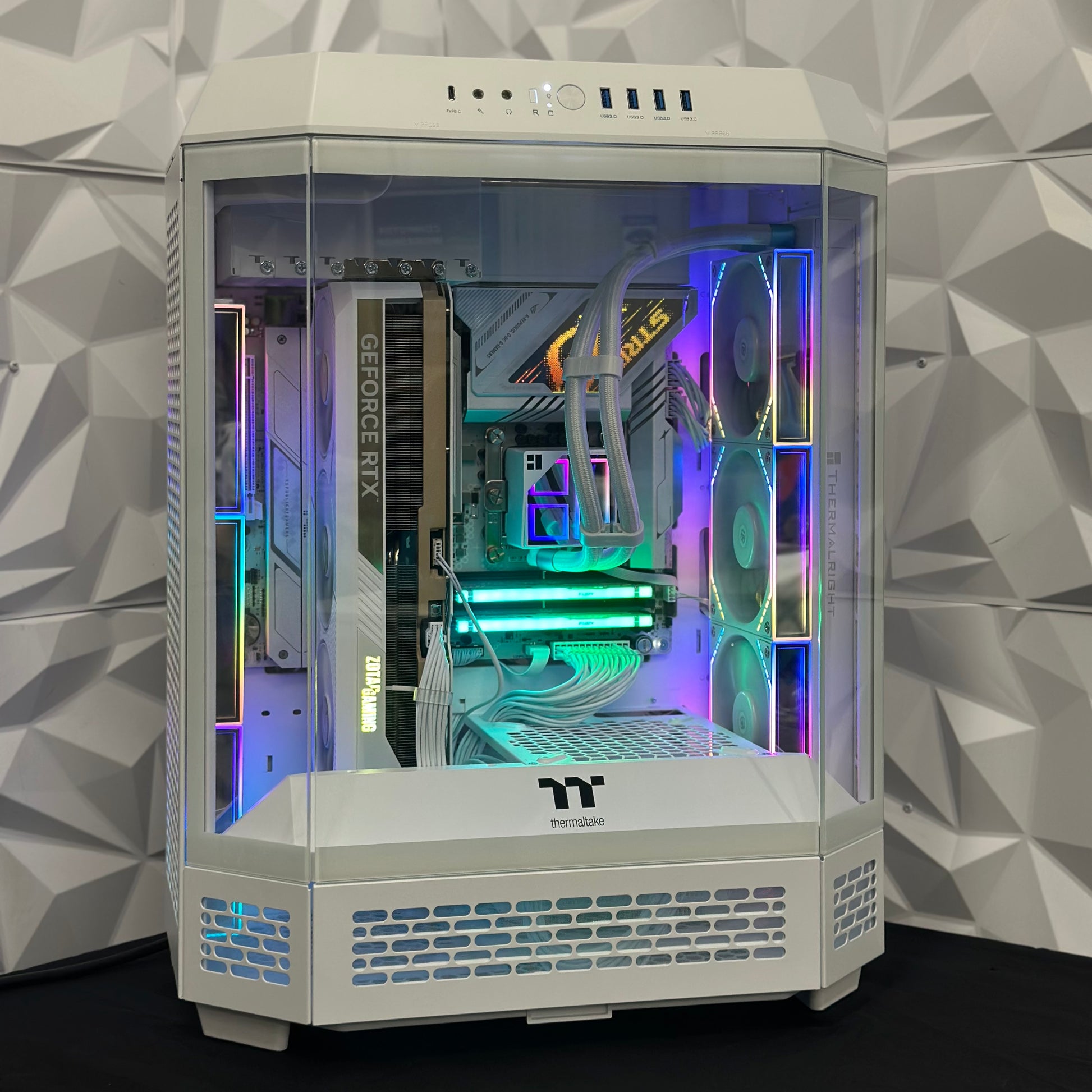 Computer gaming PC with RGB lighting in a white case against a geometric-patterned wall.