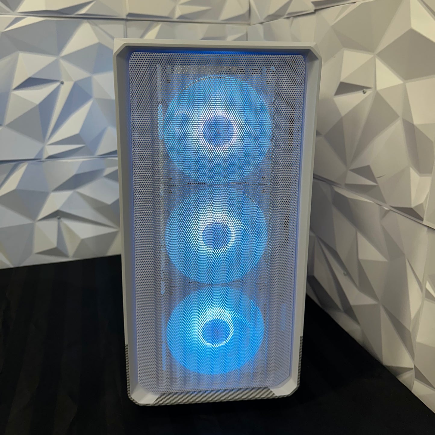 Gaming computer case with three blue LED fans against a geometric patterned wall.