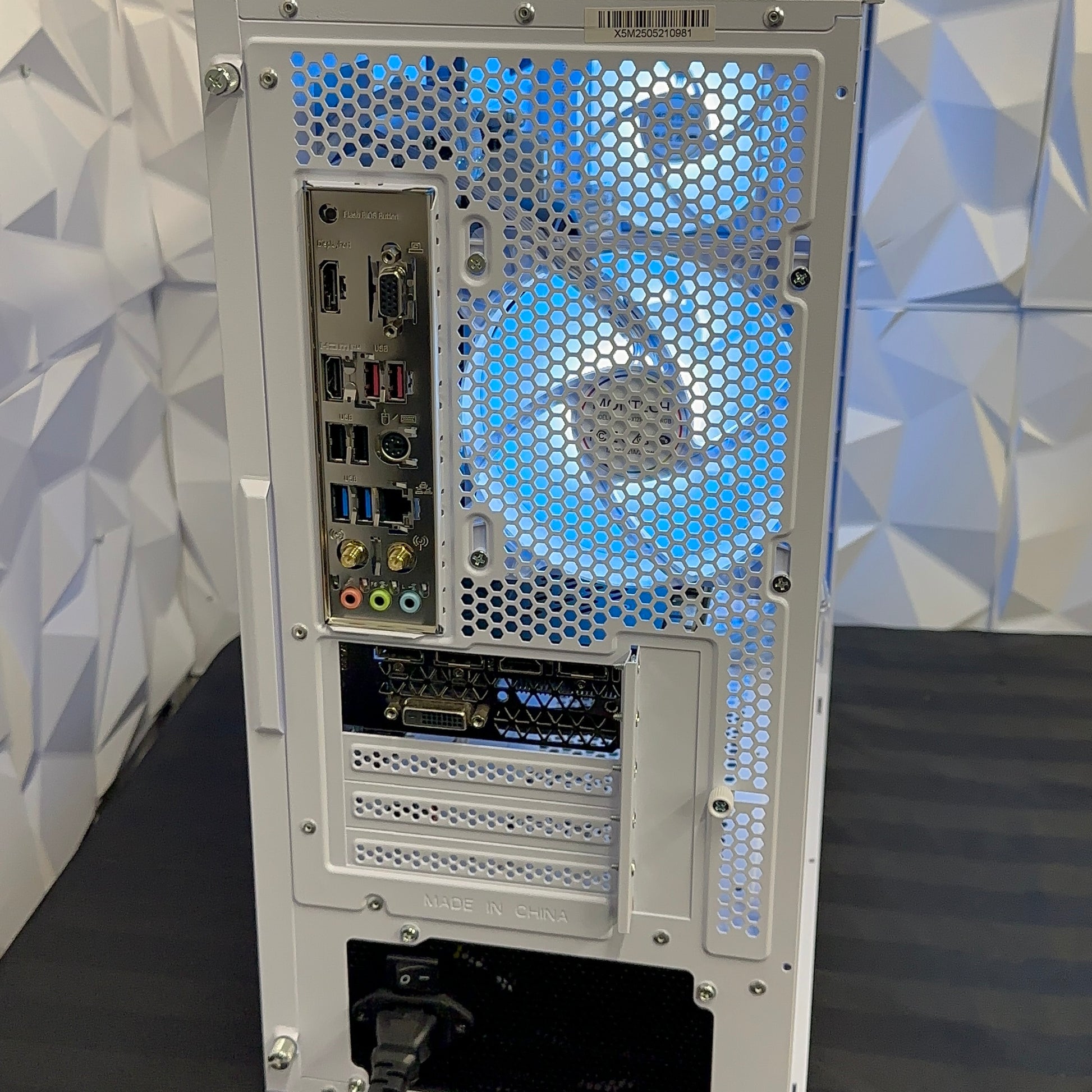 Back view of a computer case with various ports and a geometric patterned wall in the background