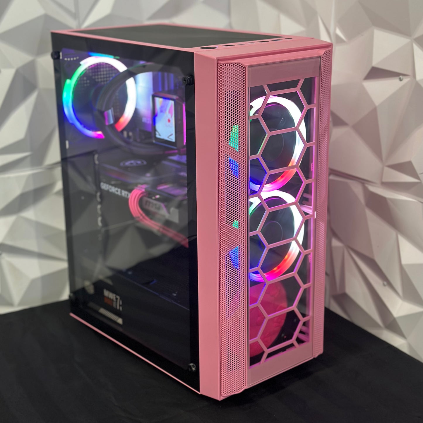 Pink computer case with RGB lighting on a geometric patterned wall background
