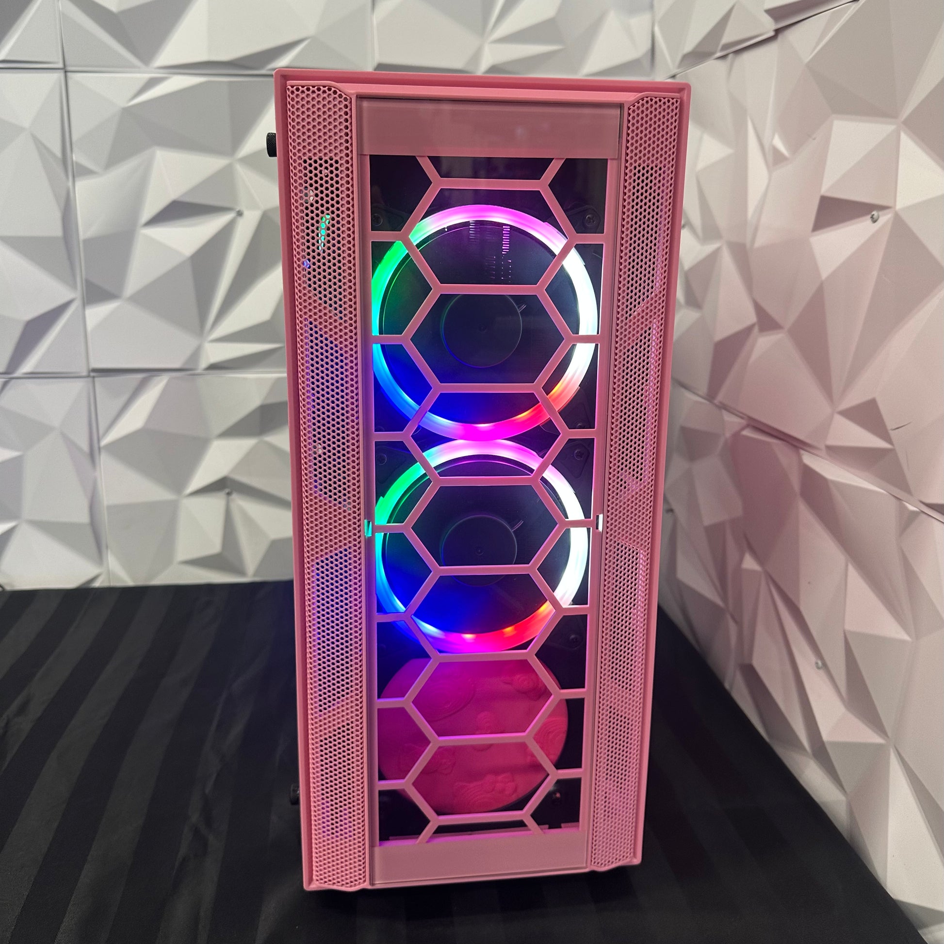 Pink computer case with RGB lighting against a geometric patterned wall.