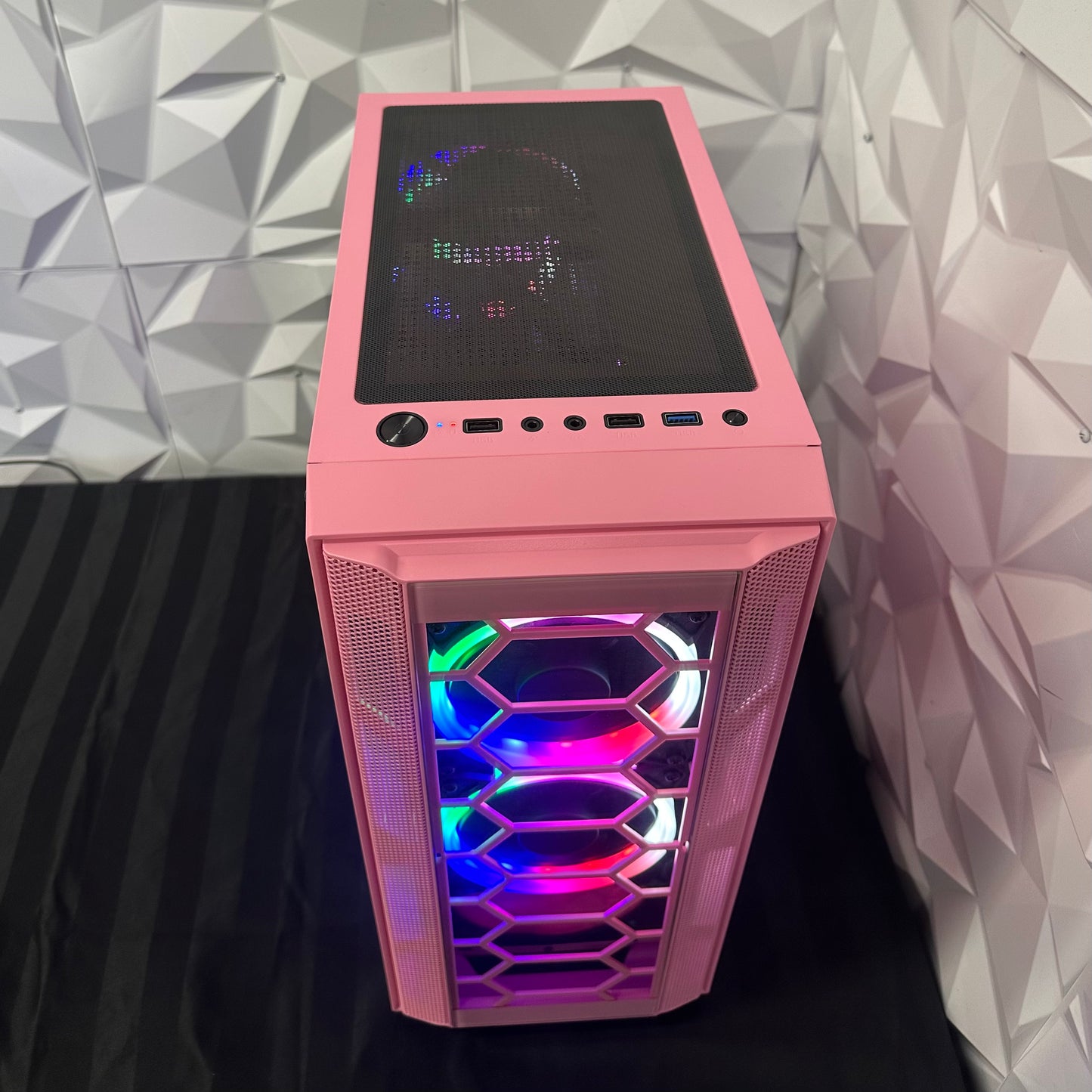 Pink computer case with RGB lighting against a geometric-patterned wall.