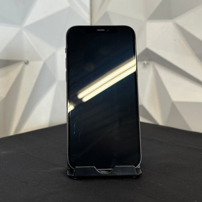 A black smartphone with a blank screen stands upright on a small display stand on a dark surface, with a geometric white wall background.