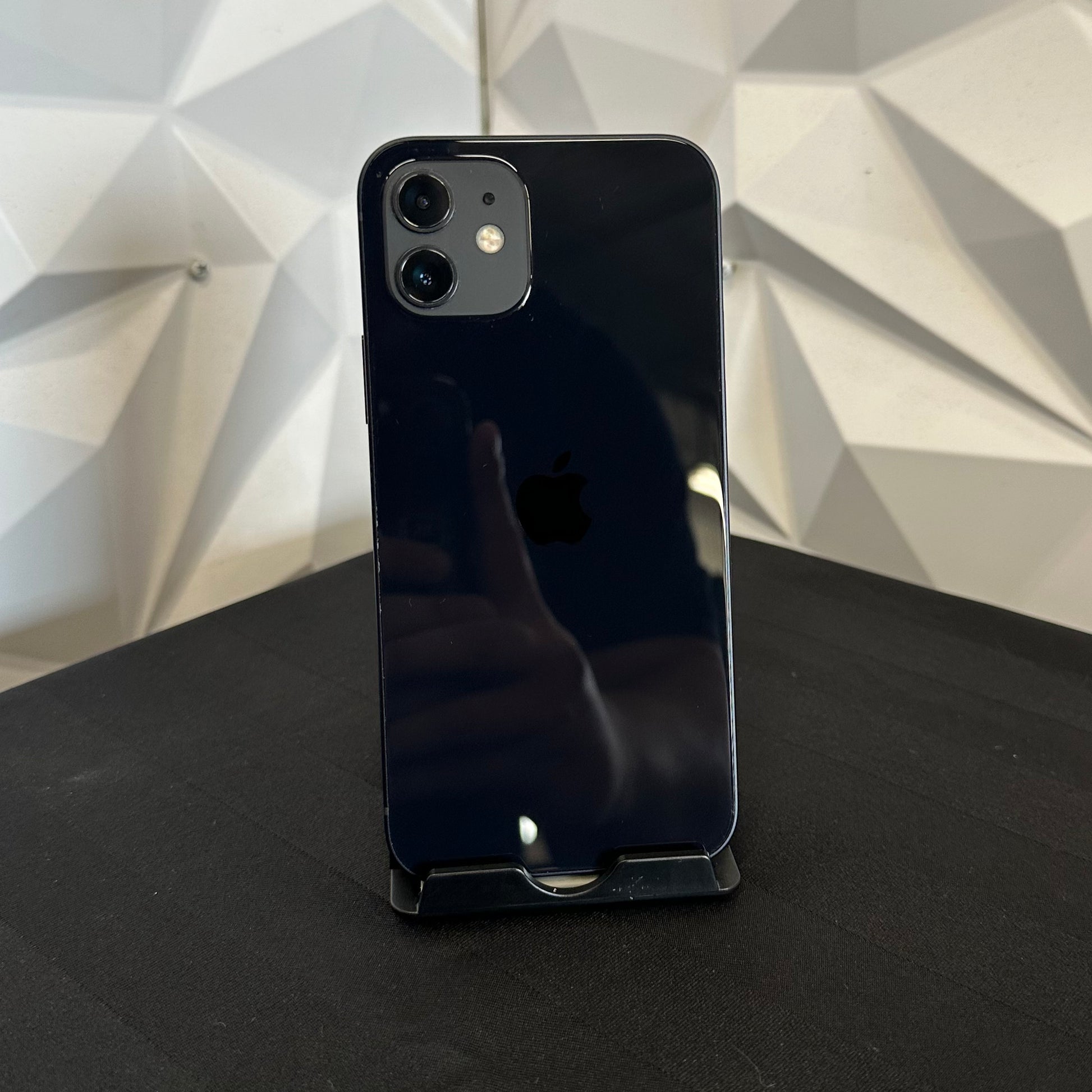A black Apple iPhone with a glossy finish stands on a black display stand. The phone is photographed from the back, showing the dual-camera cutout and the Apple logo.