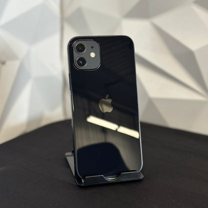 A black Apple iPhone 12 Pro shown from the back, resting on a black stand on a dark surface with a geometric white wall background.